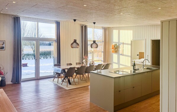 A modern kitchen with a central island, large windows, and a dining area with chairs and a table. - Awesome home in Vinderup with sauna (Vinderup)