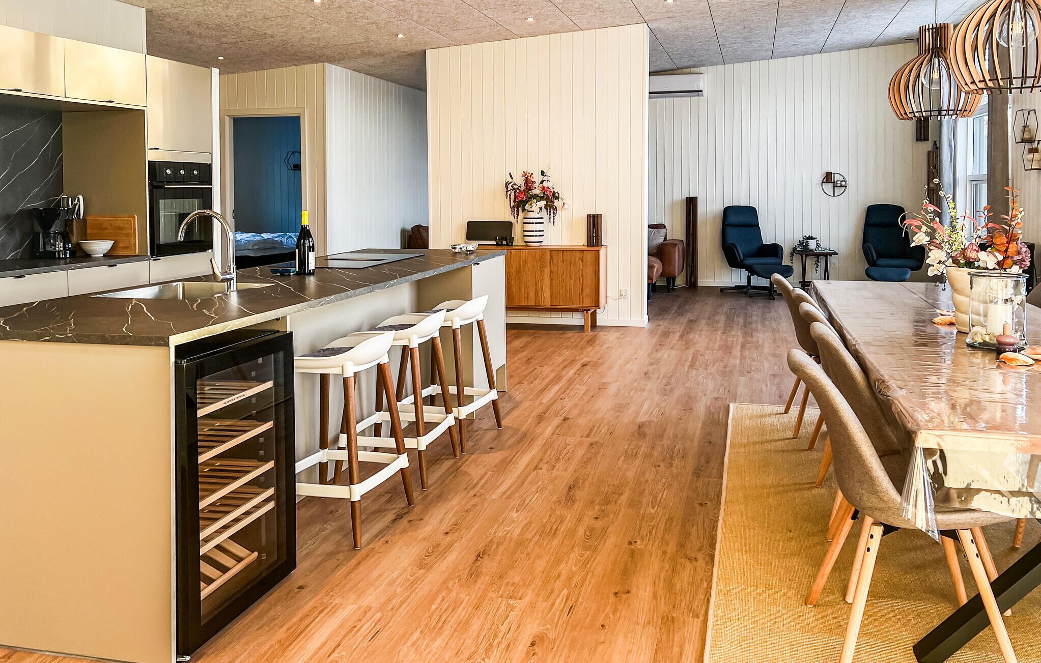 A modern kitchen with a central island, bar stools, and a dining area with a long table.