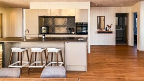 Une cuisine moderne avec un dosseret en marbre, des appareils électroménagers intégrés et un îlot central doté de tabourets de bar.