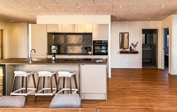 A modern kitchen with a marble backsplash, built-in appliances, and a central island with bar stools. - Awesome home in Vinderup with sauna (Vinderup)