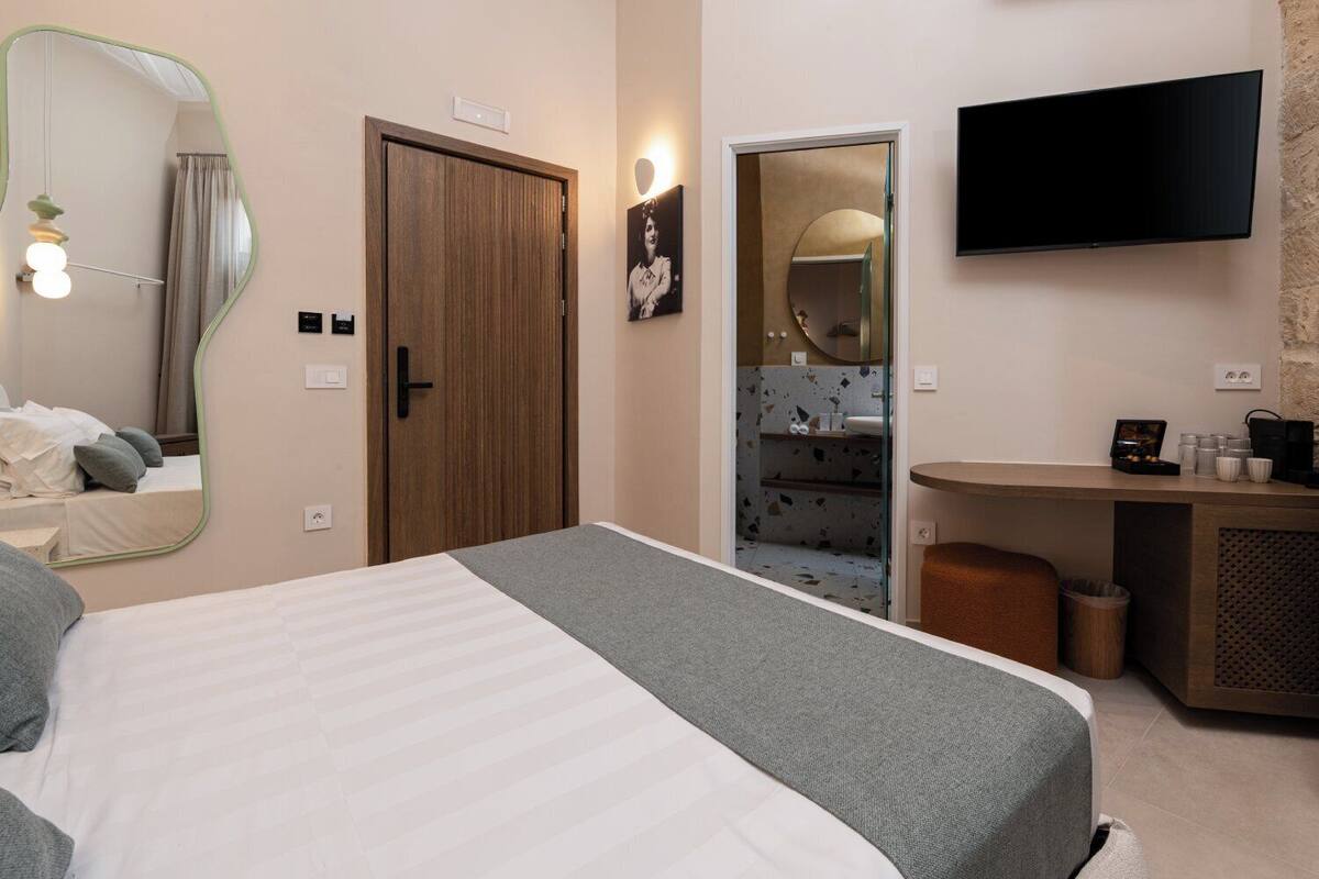 Habitación de hotel con cama, escritorio, televisión y baño visible a través de una puerta abierta.