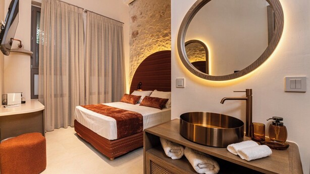 Una habitación de hotel moderna con una cama grande, un espejo redondo, un tocador de madera y una pared decorativa de piedra.