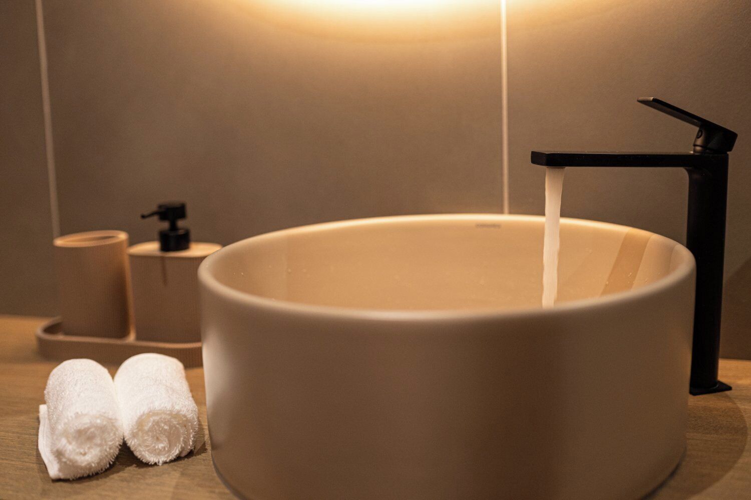 A modern bathroom with a large, round sink, a black faucet, and two rolled towels on the counter.