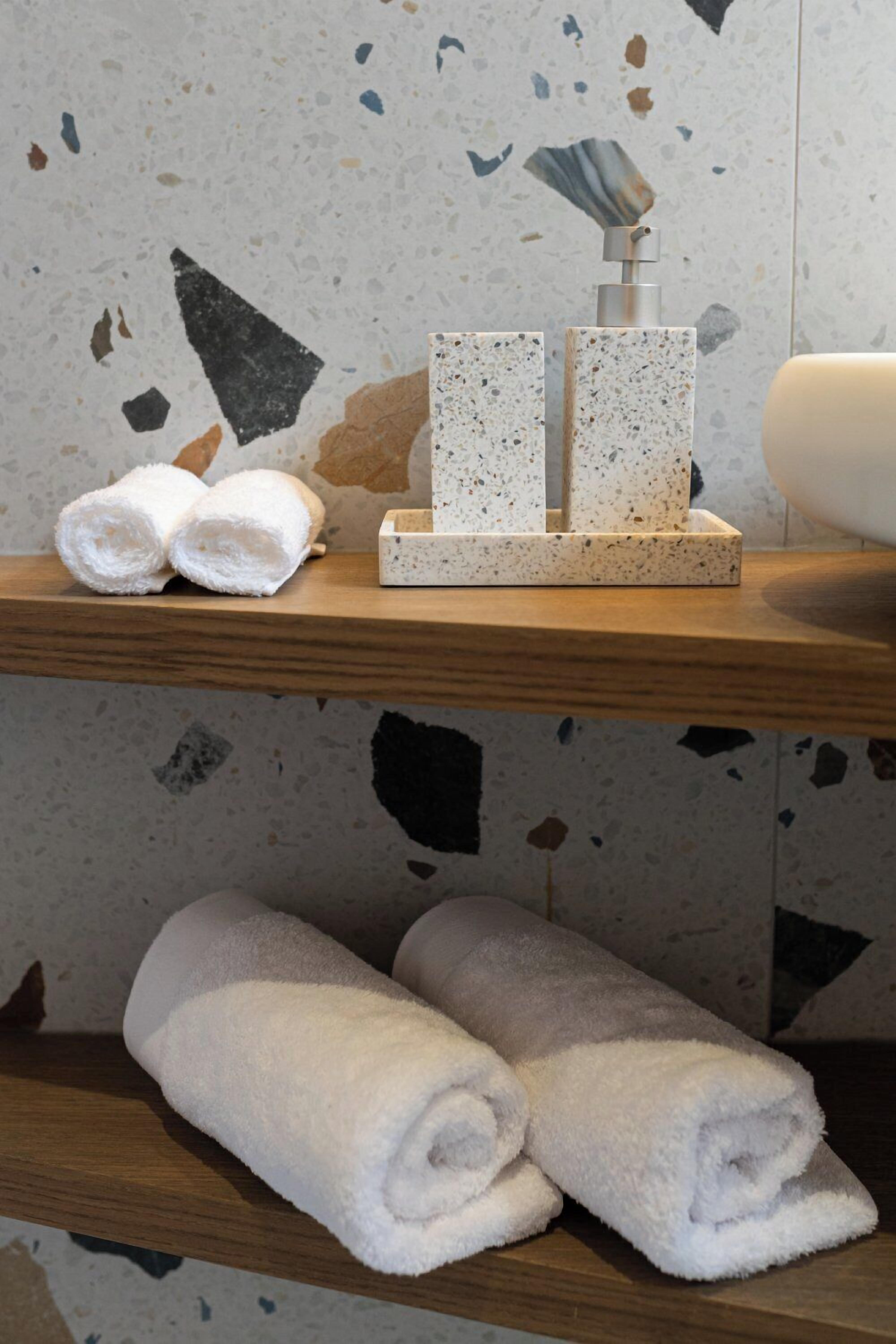 A bathroom with a wooden shelf holding rolled towels and a soap dispenser.