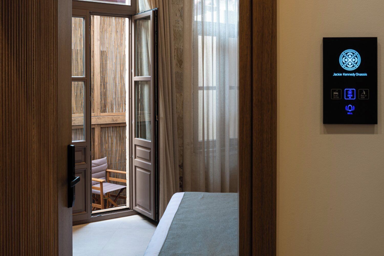 A hotel room with a sliding glass door leading to an outdoor area, a bed, a bedside table, and a control panel on the wall.