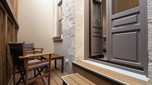 Una pequeña terraza de madera con un banco y dos sillas, un muro de piedra y una puerta con ventanal.