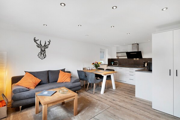 A modern living space with a grey sofa, wooden coffee table, and a dining area with a wooden table and chairs.