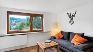 Una sala de estar moderna con un sofá gris, una mesa de centro de madera y vistas a un pueblo a través de un ventanal grande.