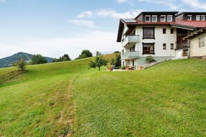 A two-story building with a balcony, situated on a grassy hill with a mountain in the background.