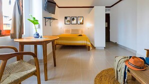 Quarto com cama, televisão na parede e uma pequena mesa com uma planta.