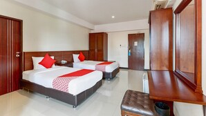 A hotel room with two beds, a wooden wardrobe, a bench, and a trash bin.