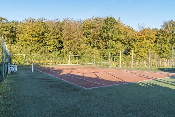 An outdoor tennis court with a net, surrounded by trees and a fence.