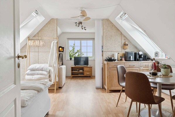 A modern loft bedroom with a bed, a TV, and a dining area with chairs and a table.