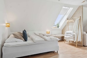 A bedroom with a bed, bedside lamps, a skylight, and a wooden floor.