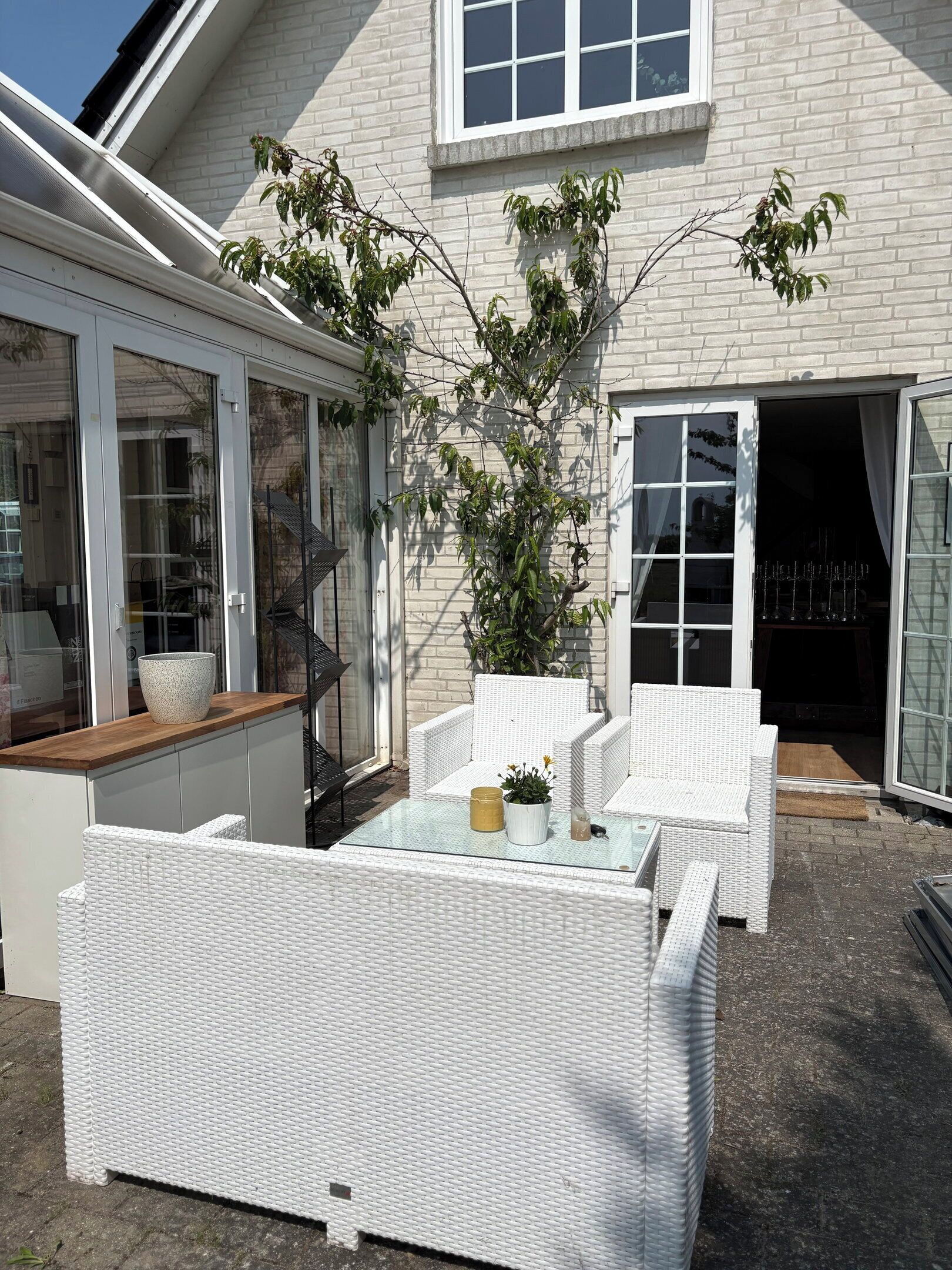 A patio area with white wicker furniture, a glass table, and a potted plant.
