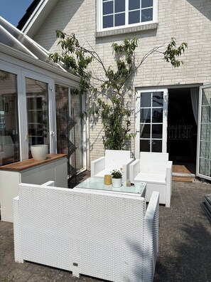 A patio area with white wicker furniture, a glass table, and a potted plant.