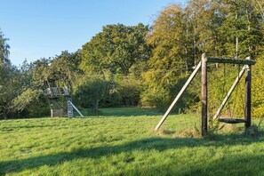 A grassy field with a wooden swing set and a treehouse structure.