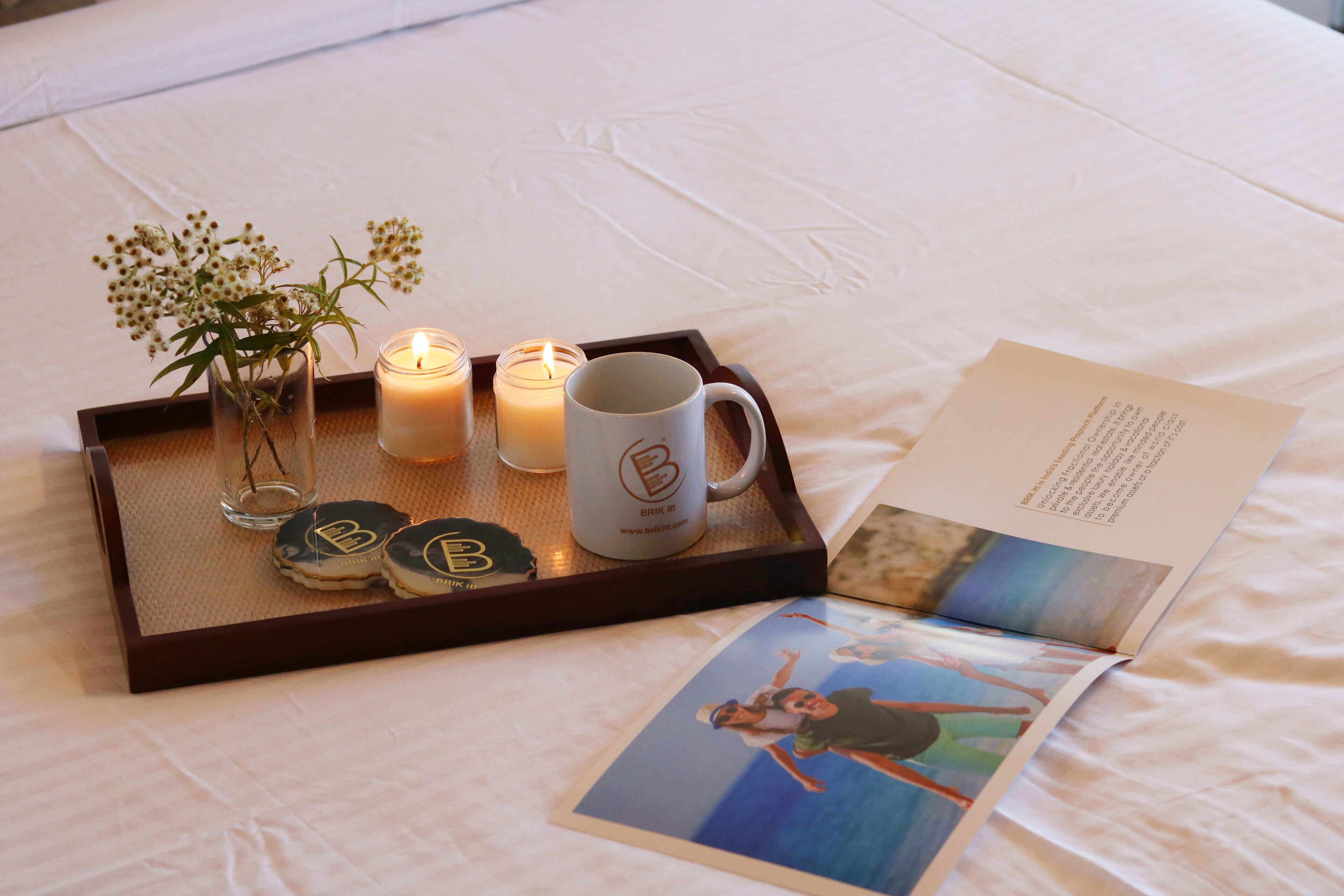 A tray with candles, a mug, and a glass vase with flowers on a bed.