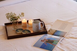 Una bandeja con velas, una taza y un florero de vidrio con flores sobre una cama.