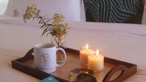 A tray with a book, a mug, candles, and a bottle opener on a bed. - BRIKitt Majestic Nirvana 2BHK Suite- Mukteshwar (South Gola Range)