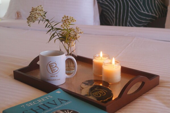 Una bandeja con un libro, una taza, velas y un abrelatas sobre la cama.