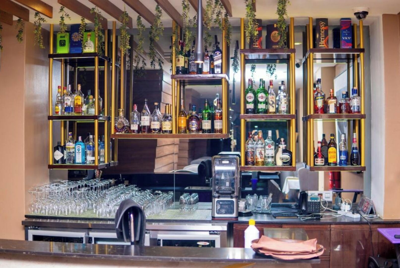 A bar area with multiple shelves of liquor bottles, a glassware rack, and a coffee machine.