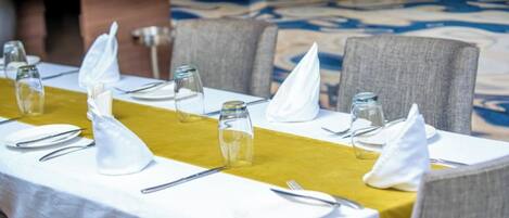 A neatly set dining table with white tablecloth, yellow runner, and grey chairs.