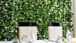 A table set with white napkins, a glass, and a bottle, against a backdrop of a green leafy wall. - Africa's Touch & Leisure (Kigali)