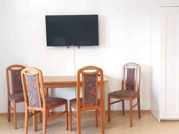 A dining area with a wooden table and four chairs with patterned upholstery. A flat-screen TV is mounted on the wall above the table.
