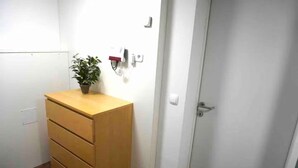 Una habitación con un aparador de madera, una planta en maceta, una puerta blanca y un enchufe en la pared.