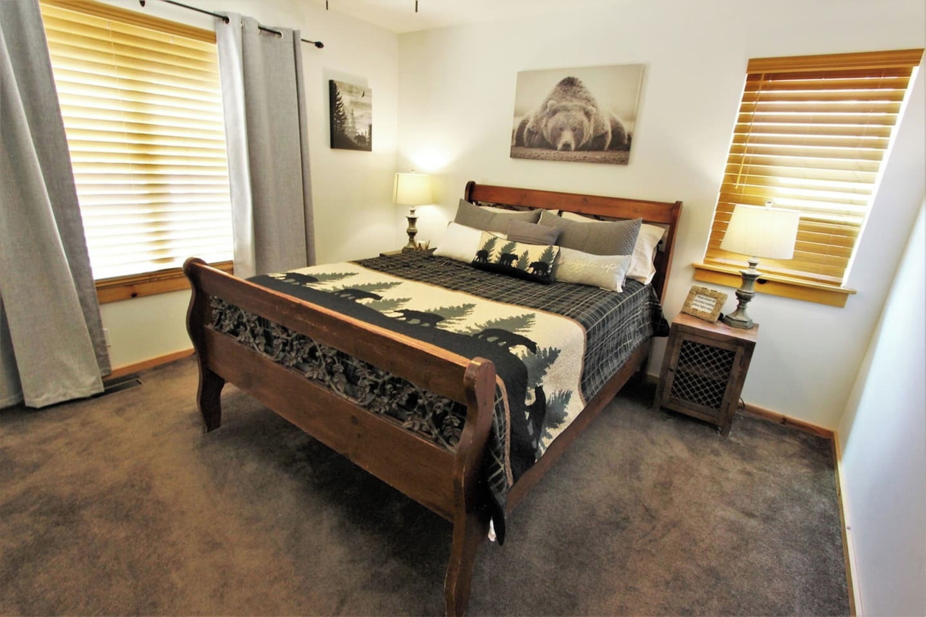 A bedroom with a wooden bed, two bedside tables, a nightstand, a lamp, and a wall-mounted picture.