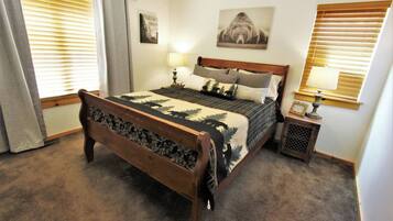 A bedroom with a wooden bed, two bedside tables, a nightstand, a lamp, and a wall-mounted picture.