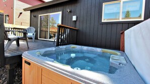 Een hottub op een houten terras, met een donker houten huis op de achtergrond.