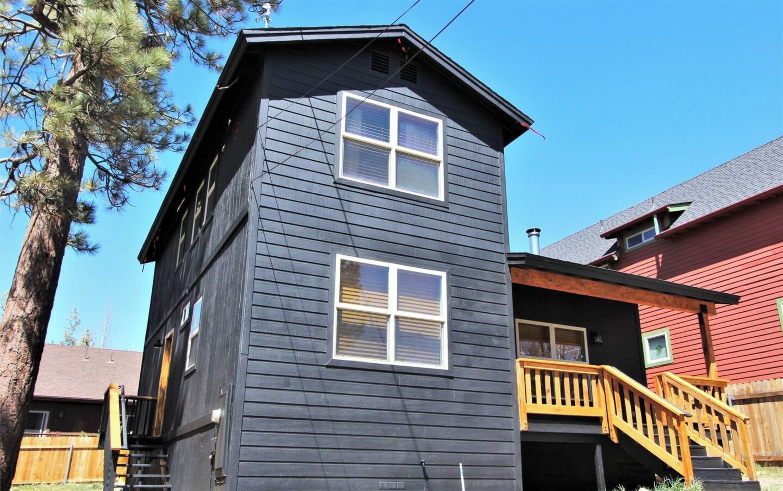A two-story building with a dark exterior, a wooden staircase leading to a deck, and a clear blue sky in the background.