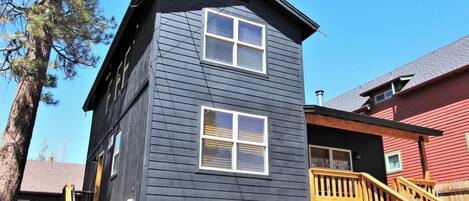 A two-story building with a dark exterior, a wooden staircase leading to a deck, and a clear blue sky in the background.