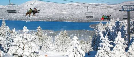 A ski lift with skiers, a lake, and snow-covered trees.