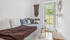 A bedroom with a bed, a bedside table, a lamp, a macrame wall hanging, and a view of greenery through a window. - Cozy home in Dronningmølle with WiFi (Dronningmølle)
