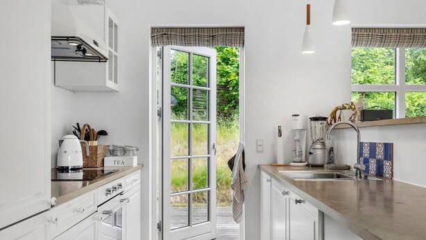 A modern kitchen with white cabinetry, a built-in oven, a coffee maker, and a blender on the counter. - Cozy home in Dronningmølle with WiFi (Dronningmølle)