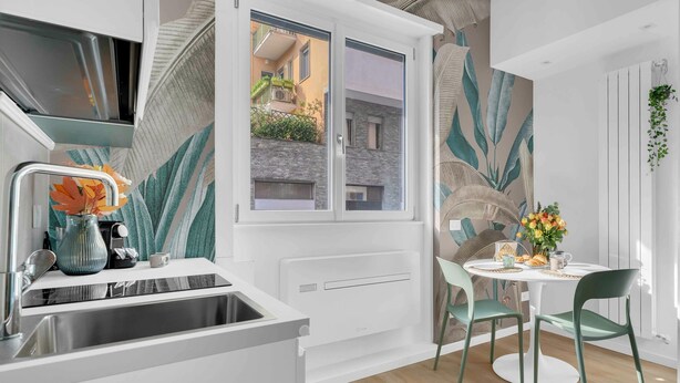 A modern kitchen with a built-in oven, a window overlooking a garden, and a dining area with a round table and chairs. - Elegant and cosy flat in Milan, closed to Fashion District, Navigli and Duomo (Milan)