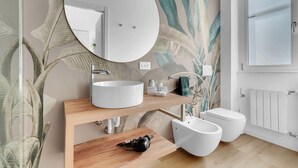 A bathroom with a round mirror, a white sink, a wooden vanity, a bidet, and a toilet. - Elegant and cosy flat in Milan, closed to Fashion District, Navigli and Duomo (Milan)