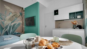 A modern room with a teal accent wall, a bed with a blue headboard, a dining table set with croissants, coffee, and a vase of flowers. - Elegant and cosy flat in Milan, closed to Fashion District, Navigli and Duomo (Milan)
