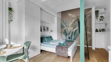 A modern bedroom with a bed, a desk, and chairs. There are plants and artwork on the walls.