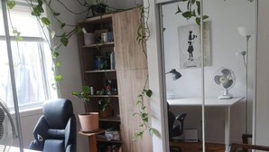 Een moderne kantoorruimte met een houten vloer, een wit bureau, een zwarte kantoorstoel, een boekenkast en een potplant.