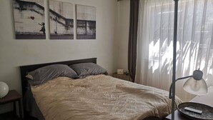 Een slaapkamer met een bed, een nachtkastje, een lamp en kunst aan de muur.