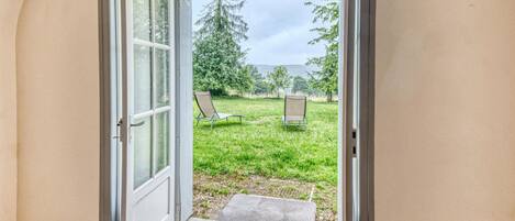Een open deur die leidt naar een grasveld met twee stoelen en een gestructureerde mat bij de ingang.
