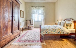 A bedroom with a wooden bed, a chair, a large wardrobe, and a window with curtains.