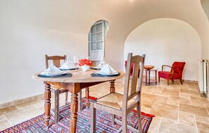 A dining area with a round wooden table set for four, surrounded by wooden chairs. A red chair is placed at the far end of the table.