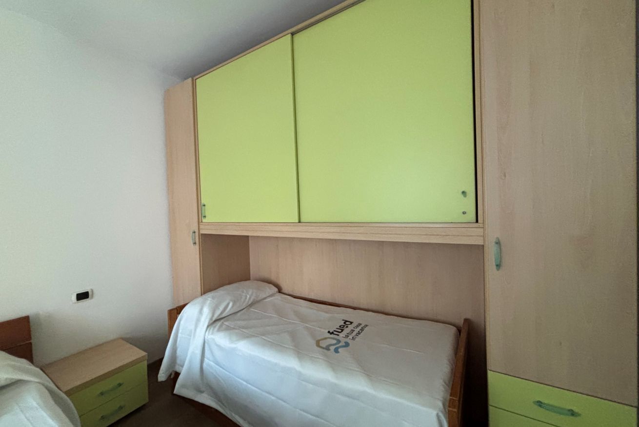 A bedroom with a bed, a nightstand, a green wardrobe, and a small cabinet.