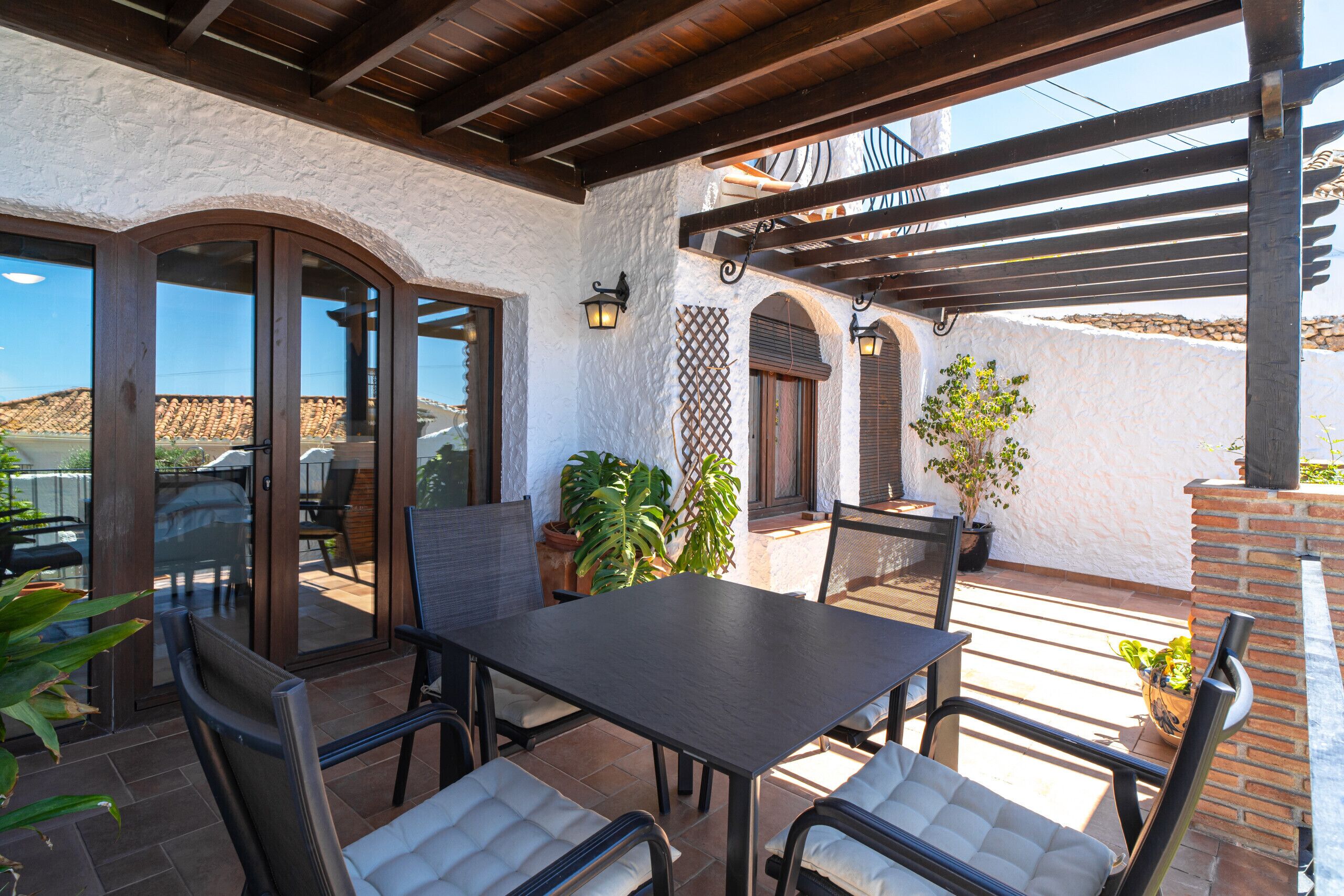 Un patio al aire libre con una mesa, sillas, plantas en macetas y una pérgola.