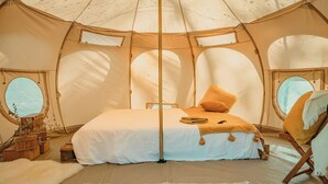 Una carpa espaciosa con una cama grande, una silla de madera y una mesita con objetos decorativos.